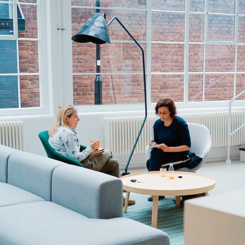 two woman sits on sofa chairs inside house